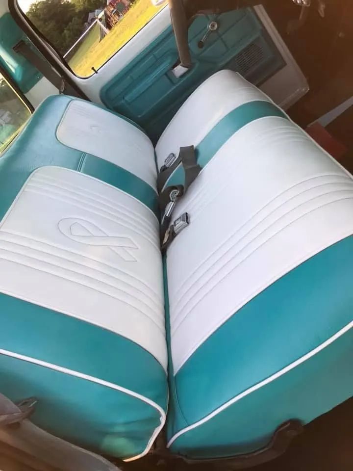 Two-tone white and teal car seats with white piping and a ribbon emblem, seen from above.