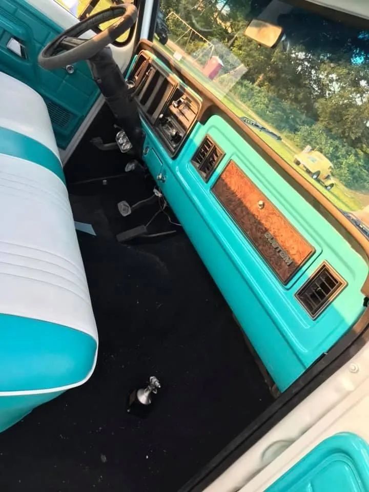 Interior of a classic turquoise and white pickup truck, including dashboard, steering wheel, and bench seat.