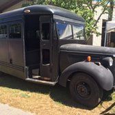 Black vintage school bus with open door, parked outdoors on grass.
