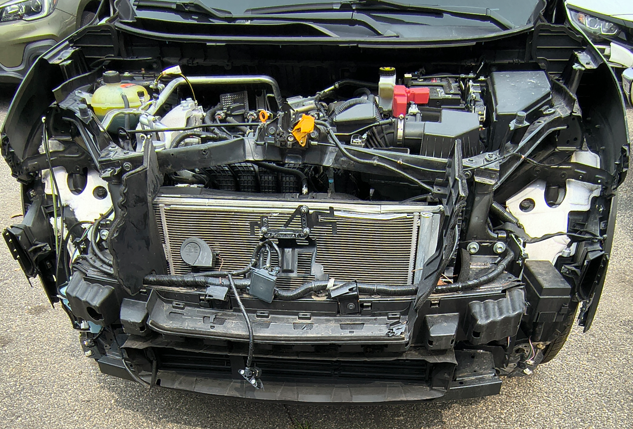 Damaged black car front: grill, engine visible, headlights missing.