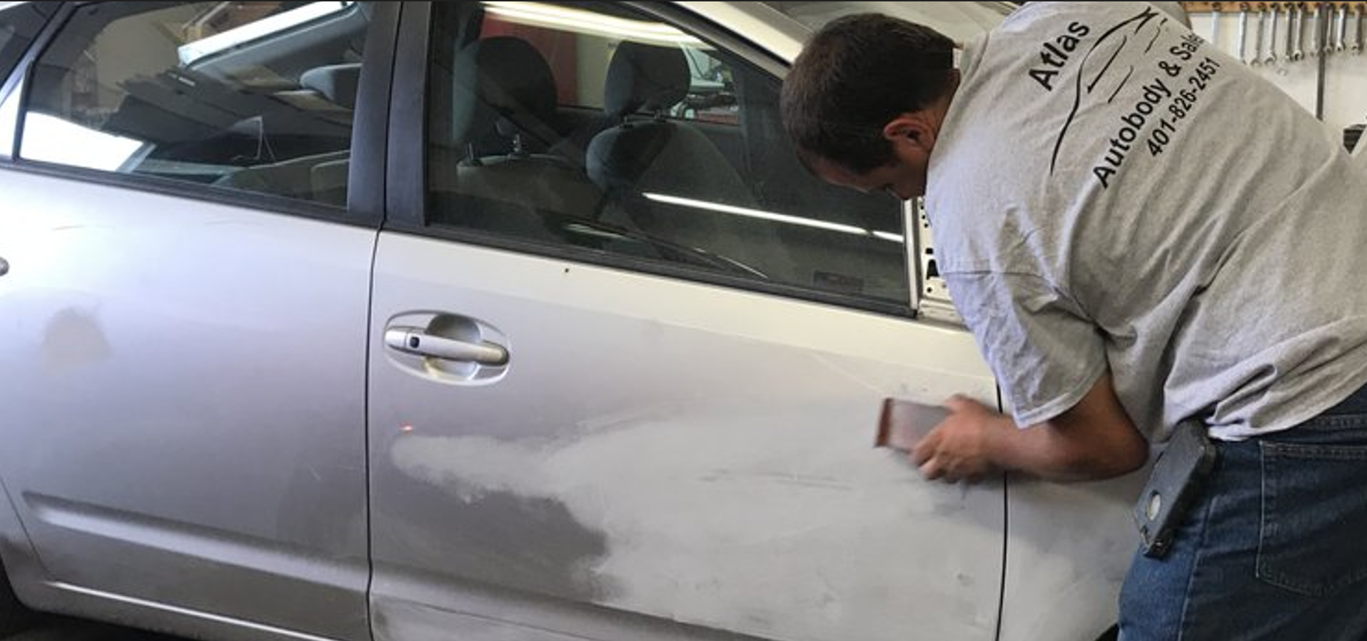 A person sanding a car door in an auto body shop.