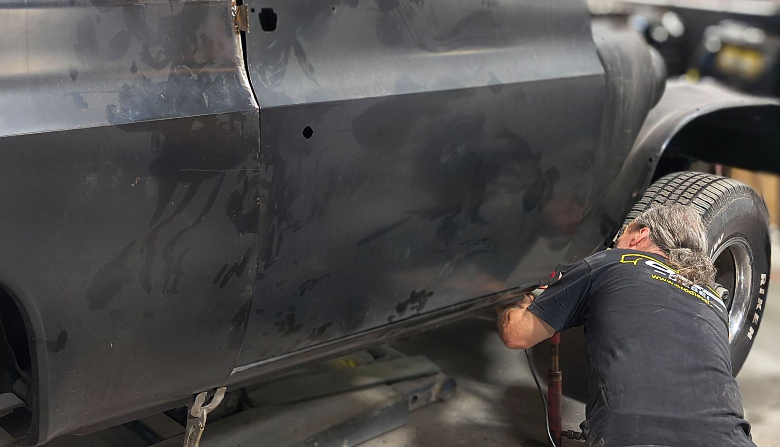 A person working on the side panel of a dark vehicle in a shop.