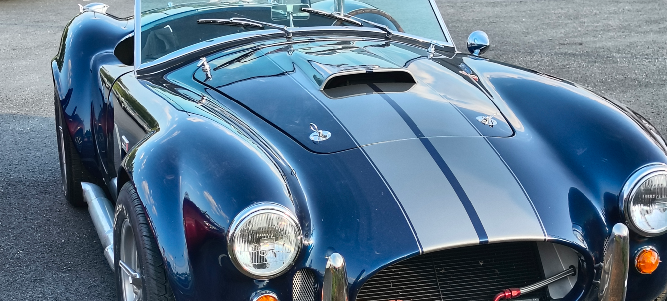 Blue and silver Shelby Cobra sports car with white racing stripes.