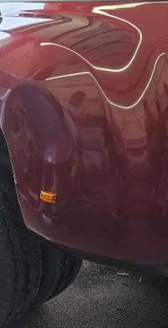 Maroon classic car fender with orange side marker, tire visible, reflective light.
