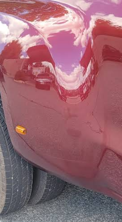Red truck body reflecting sky and clouds, with tires and amber light visible.