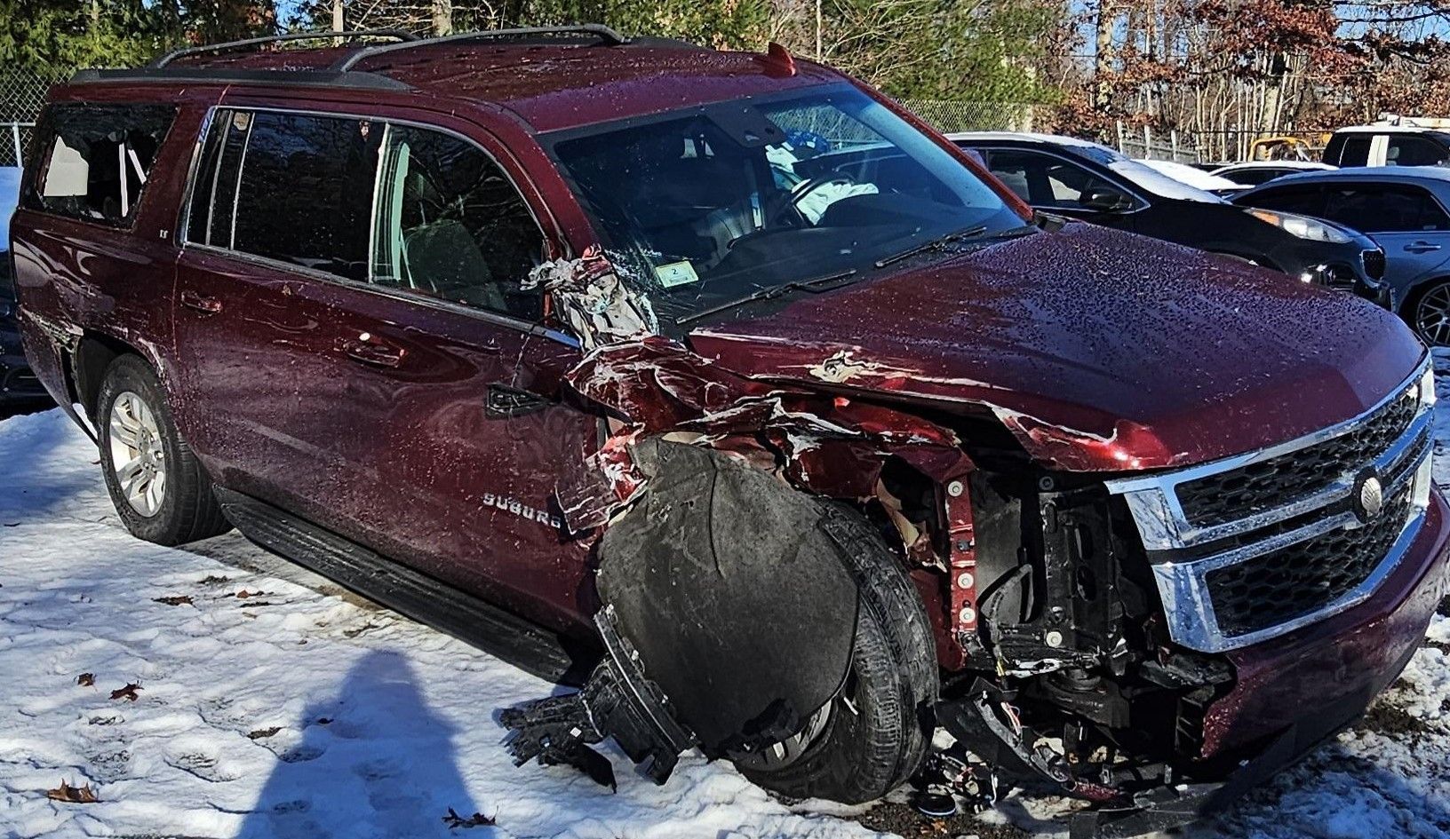 Damaged burgundy SUV with front-end collision; tire blown, snow on ground.