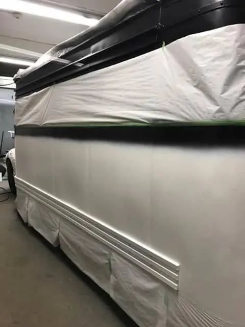 White bus exterior, partially covered, inside a workshop; fresh paint, trim details.