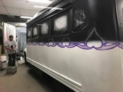 Man painting a white RV with a purple heart design in a workshop.