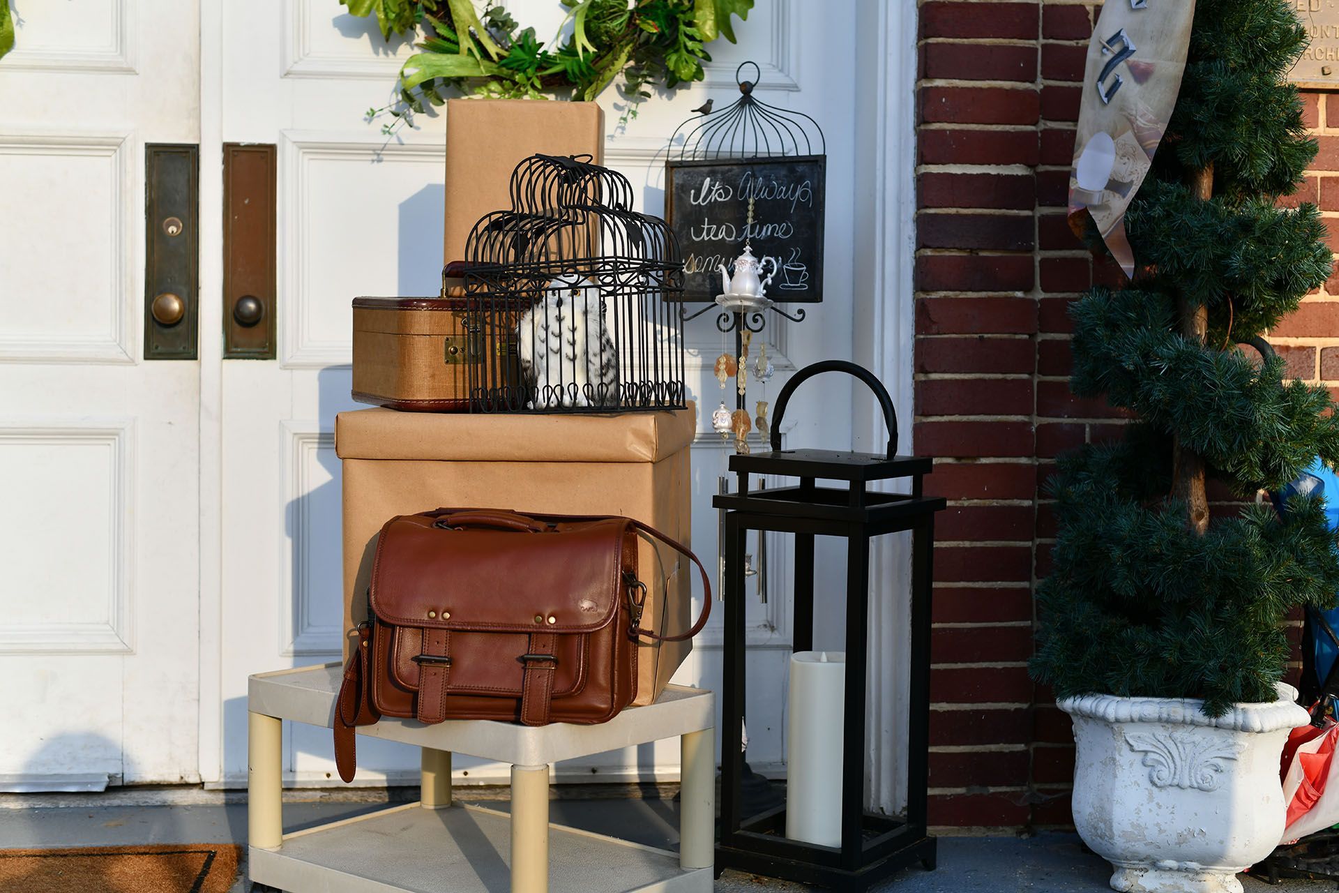 Front door decorated with packages, birdcages, lantern, leather bag, and topiary