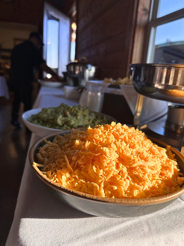 A bowl of shredded cheese is sitting on a table next to a bowl of guacamole.