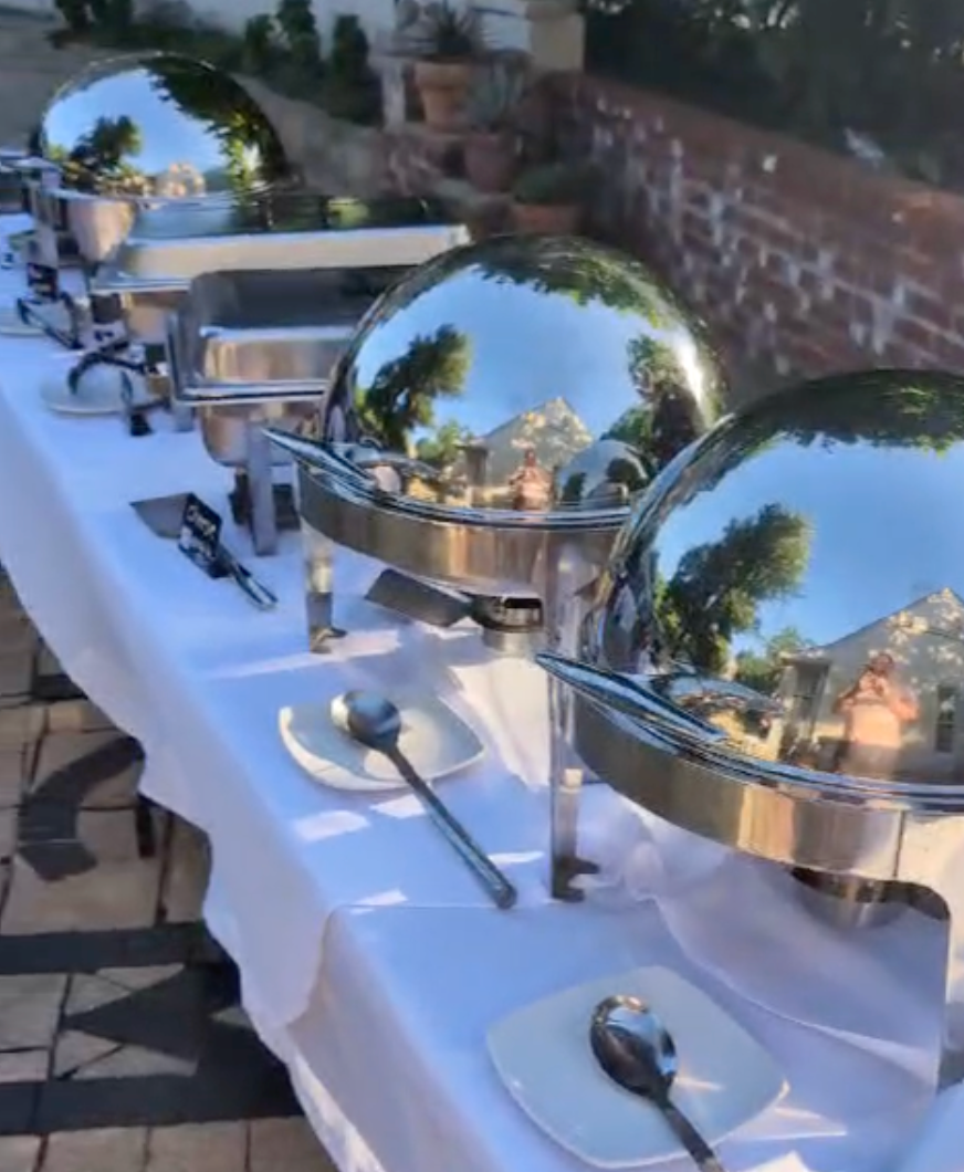 A long table topped with stainless steel buffet dishes and utensils.