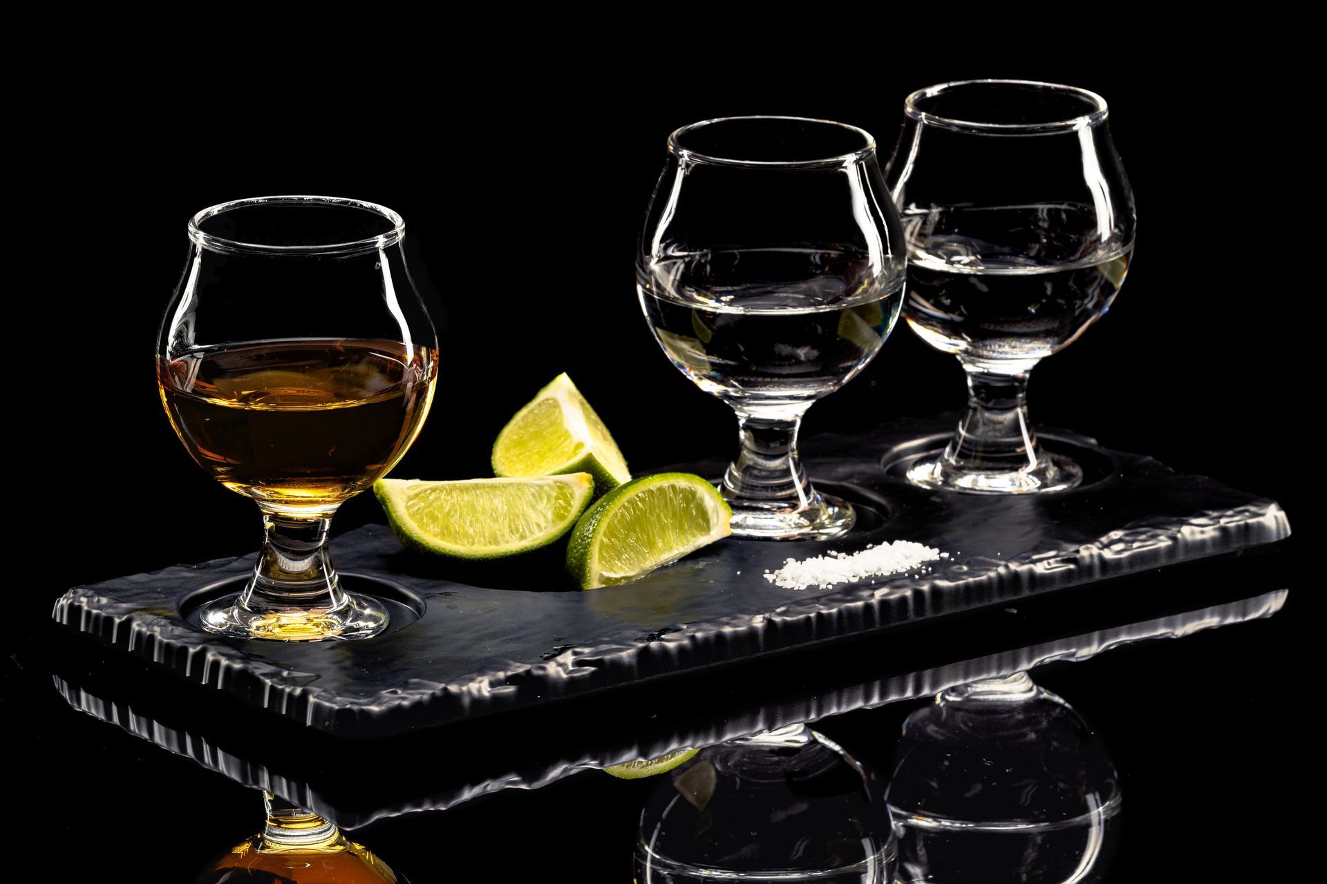 two glasses of tequila, a slice of lime, and salt on a tray