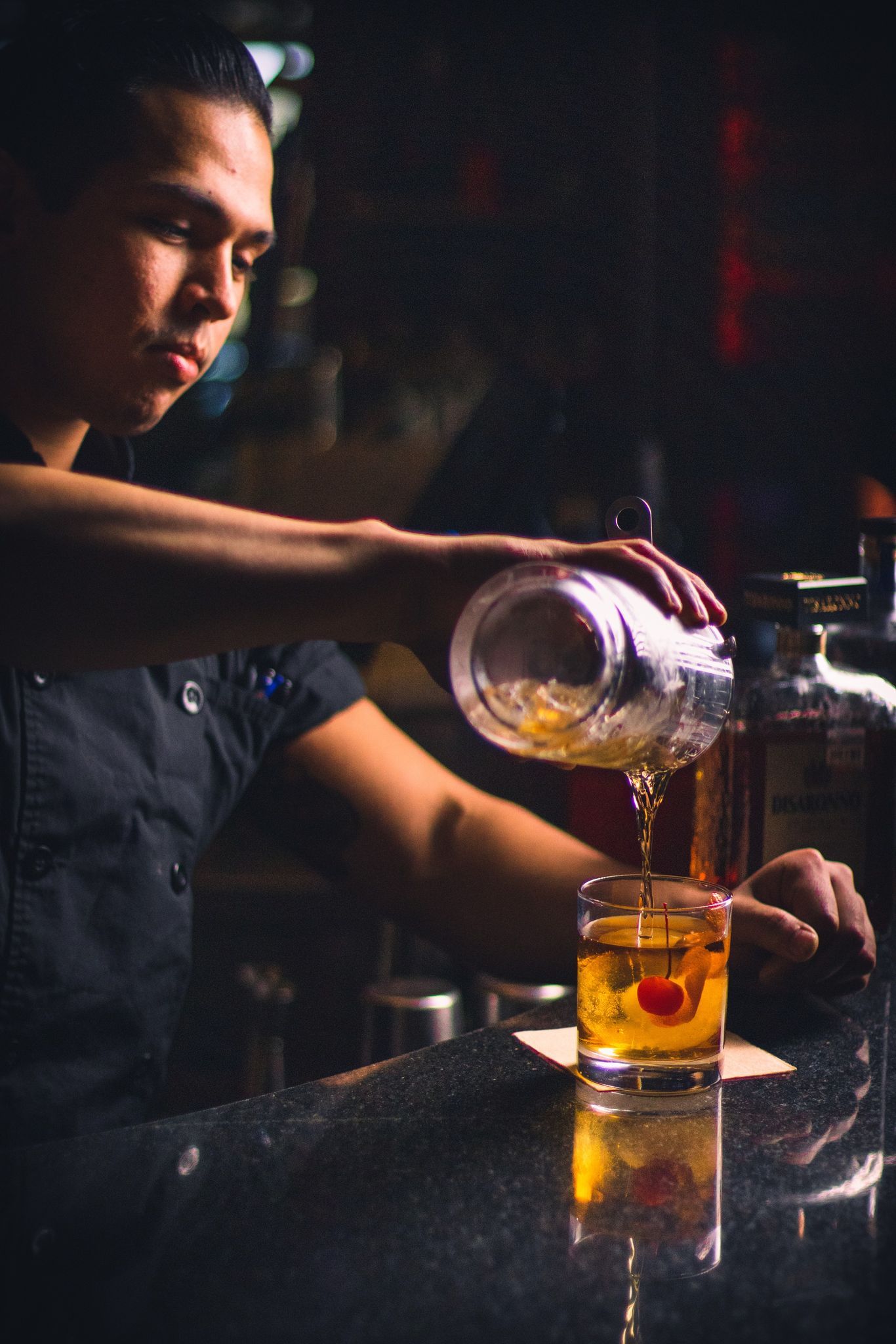 a bartender is pouring a drink into a glass with a cherry in it