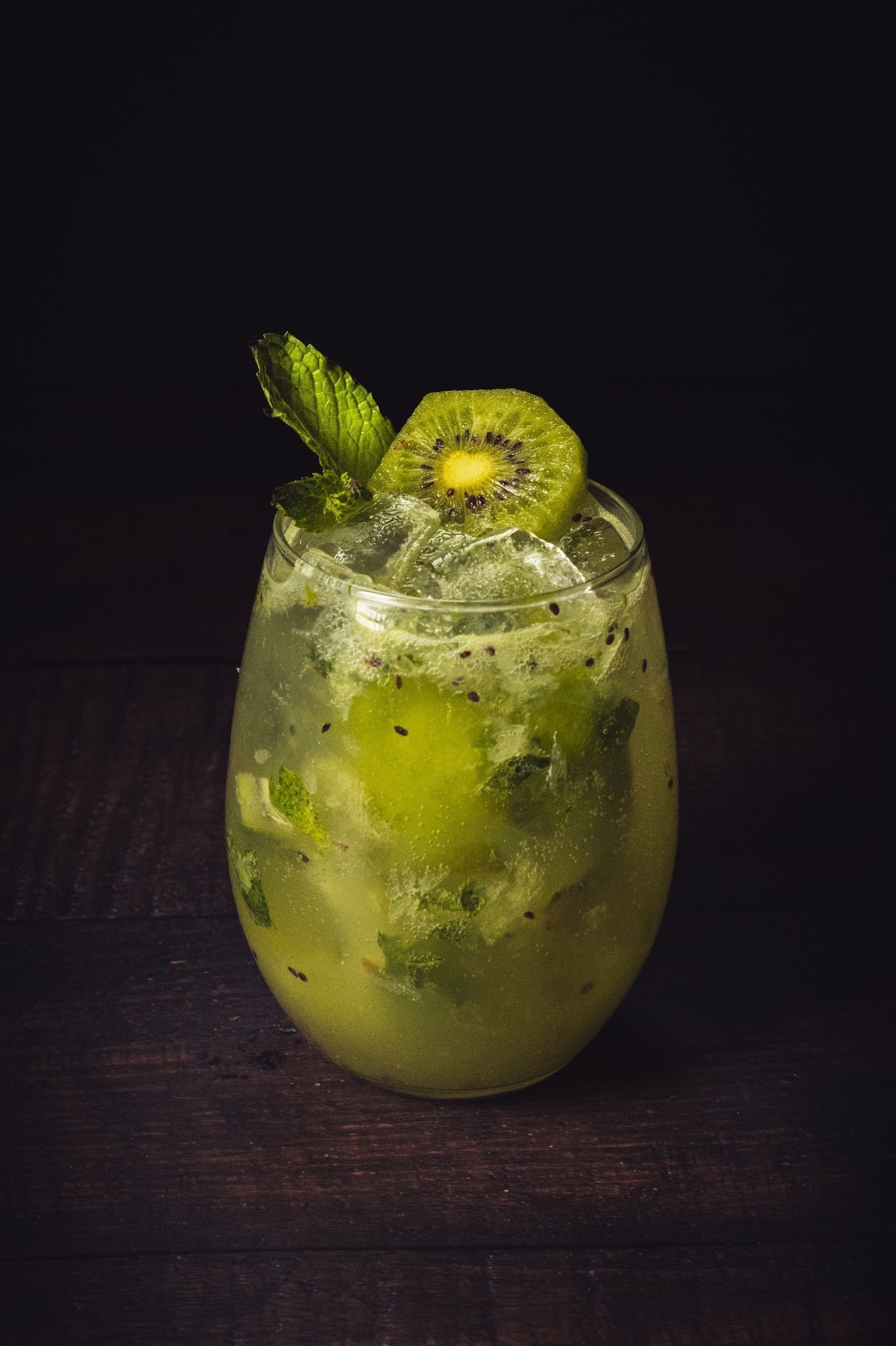 a close up of a kiwi mojito in a glass on a wooden table