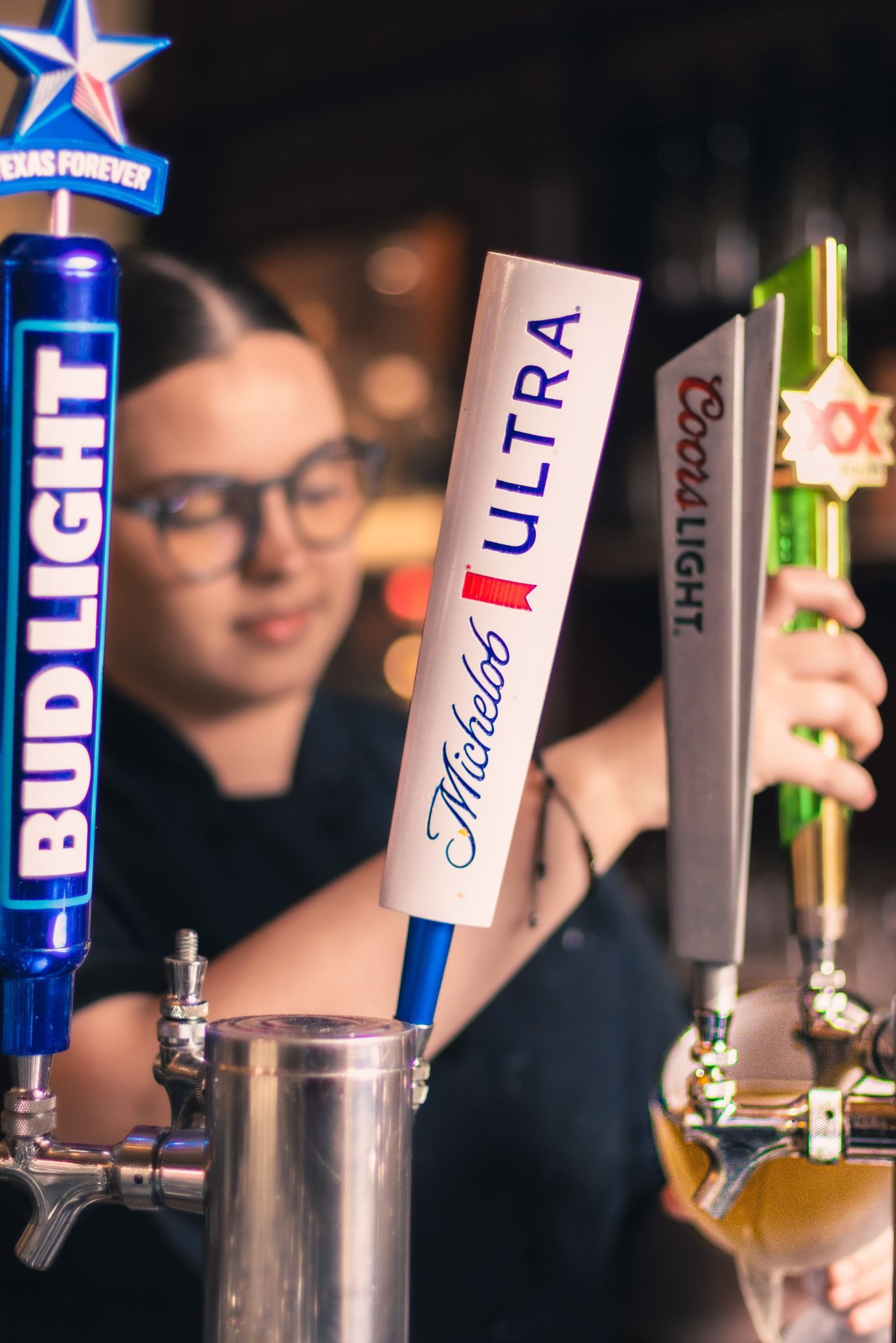 a woman is pouring beer from a tap that says bud light on it