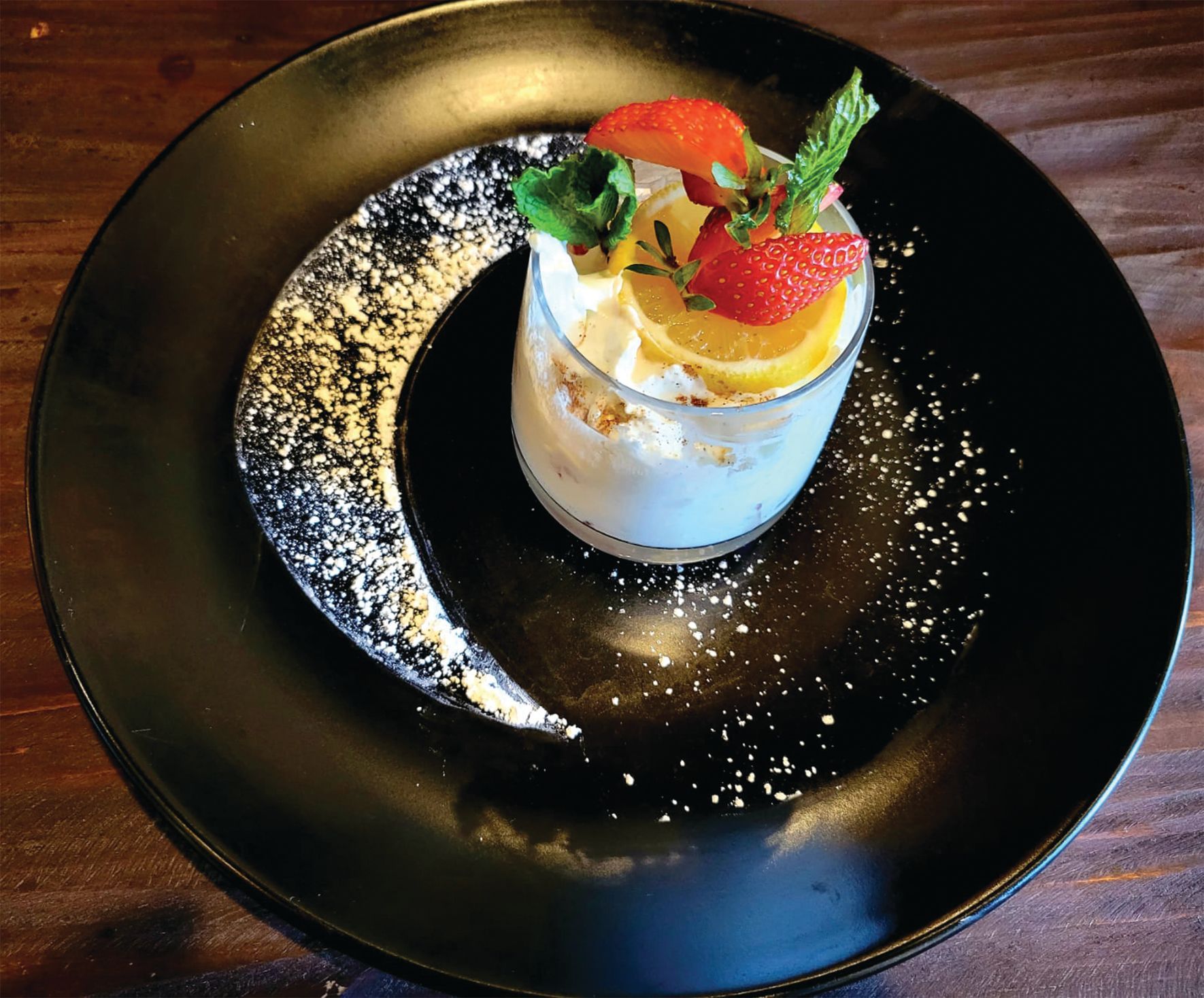 a dessert with strawberries and lemons on a black plate