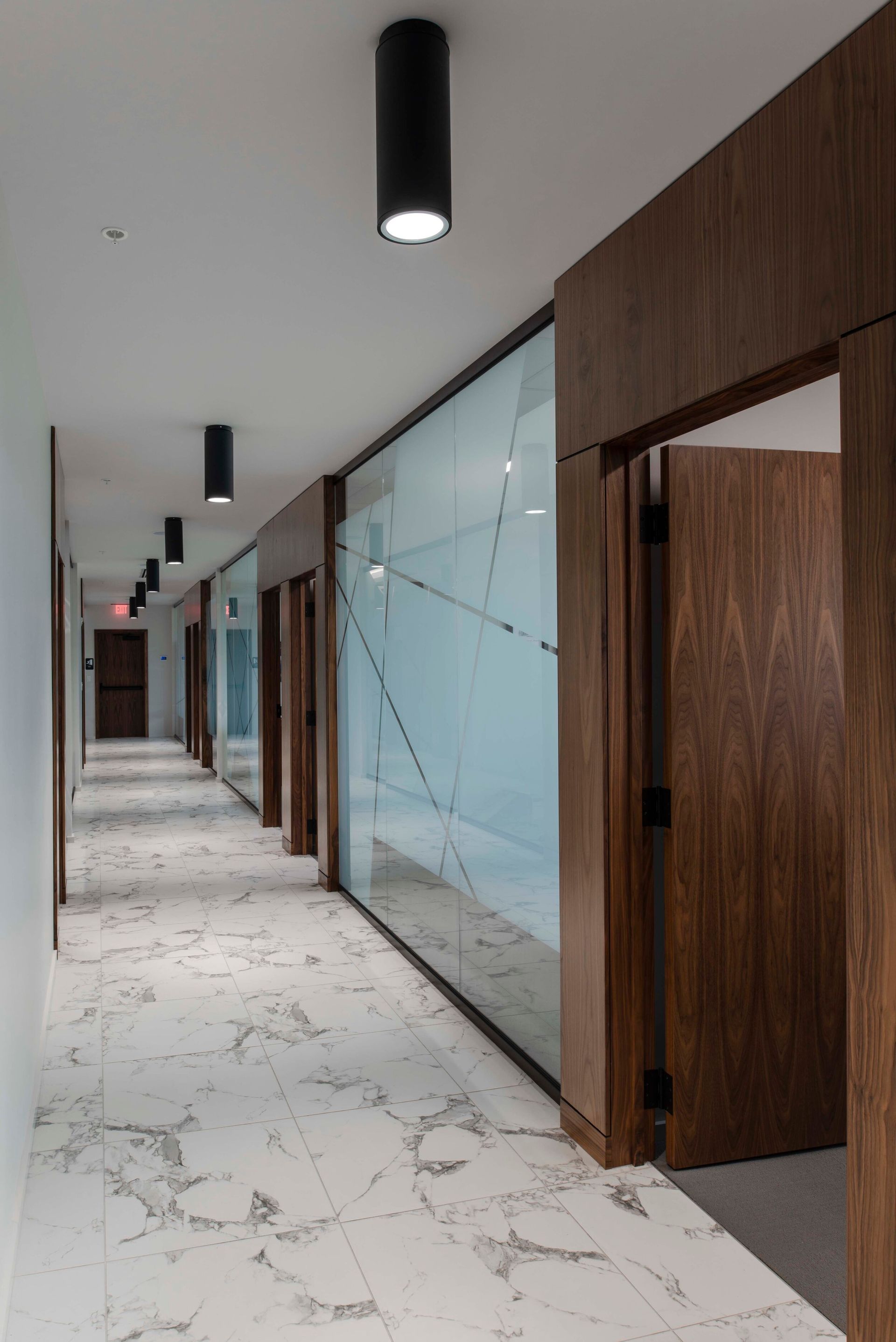 Hallway with patterned marble floor, wooden doors, frosted glass wall, and black cylindrical lights.