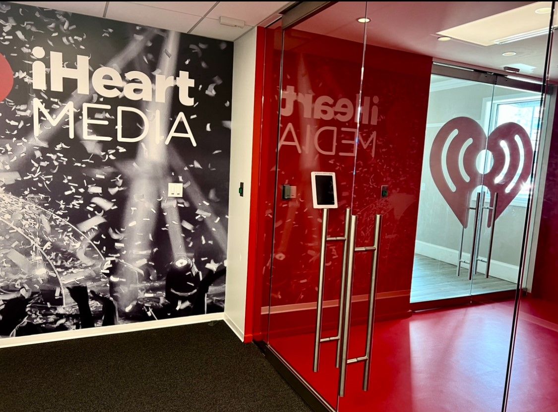 Entry to iHeartMedia office with red and black accents, glass door, logo, and heart design.