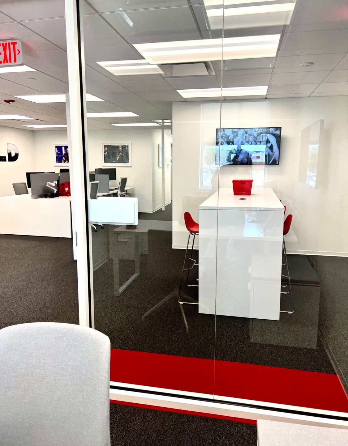 Office interior with a white table, red chairs, and a TV. Red, black, and white carpet.