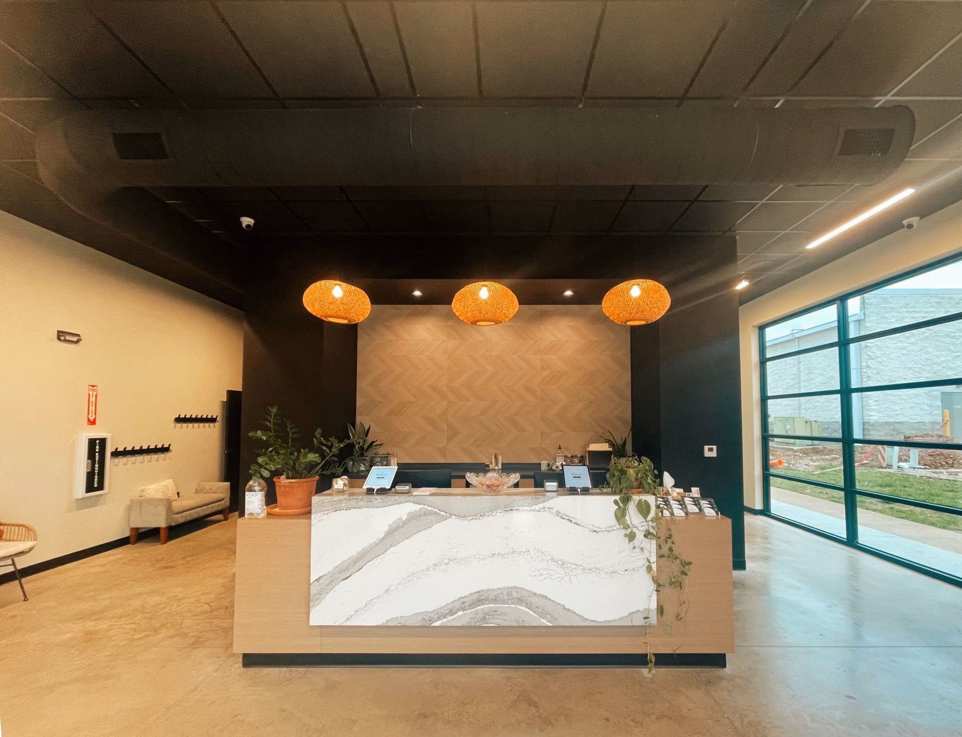 Reception area with a modern design. Beige desk with a mosaic front, plants, and three orange globe lights.
