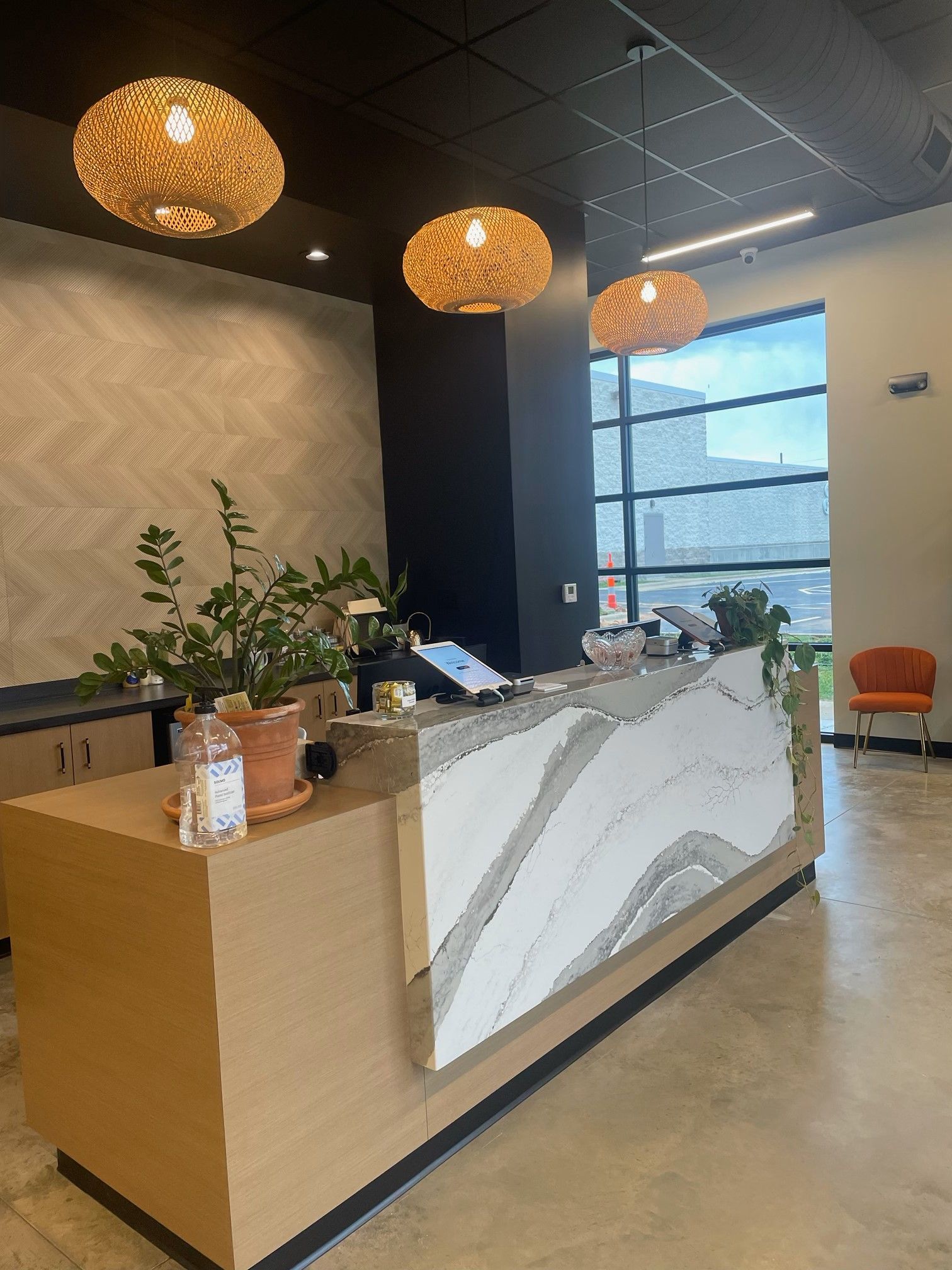 Reception desk with woven pendant lights, stone countertop, and potted plants.