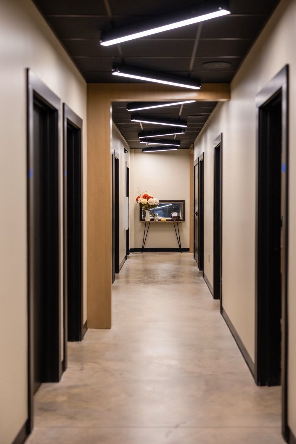 Long, narrow hallway with closed black doors, cream walls, and a black ceiling with linear lights.