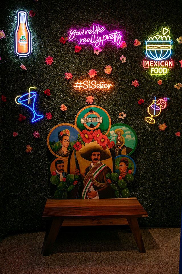 Mexican restaurant photo booth with neon signs and portraits of Mexican figures. Includes wooden bench.