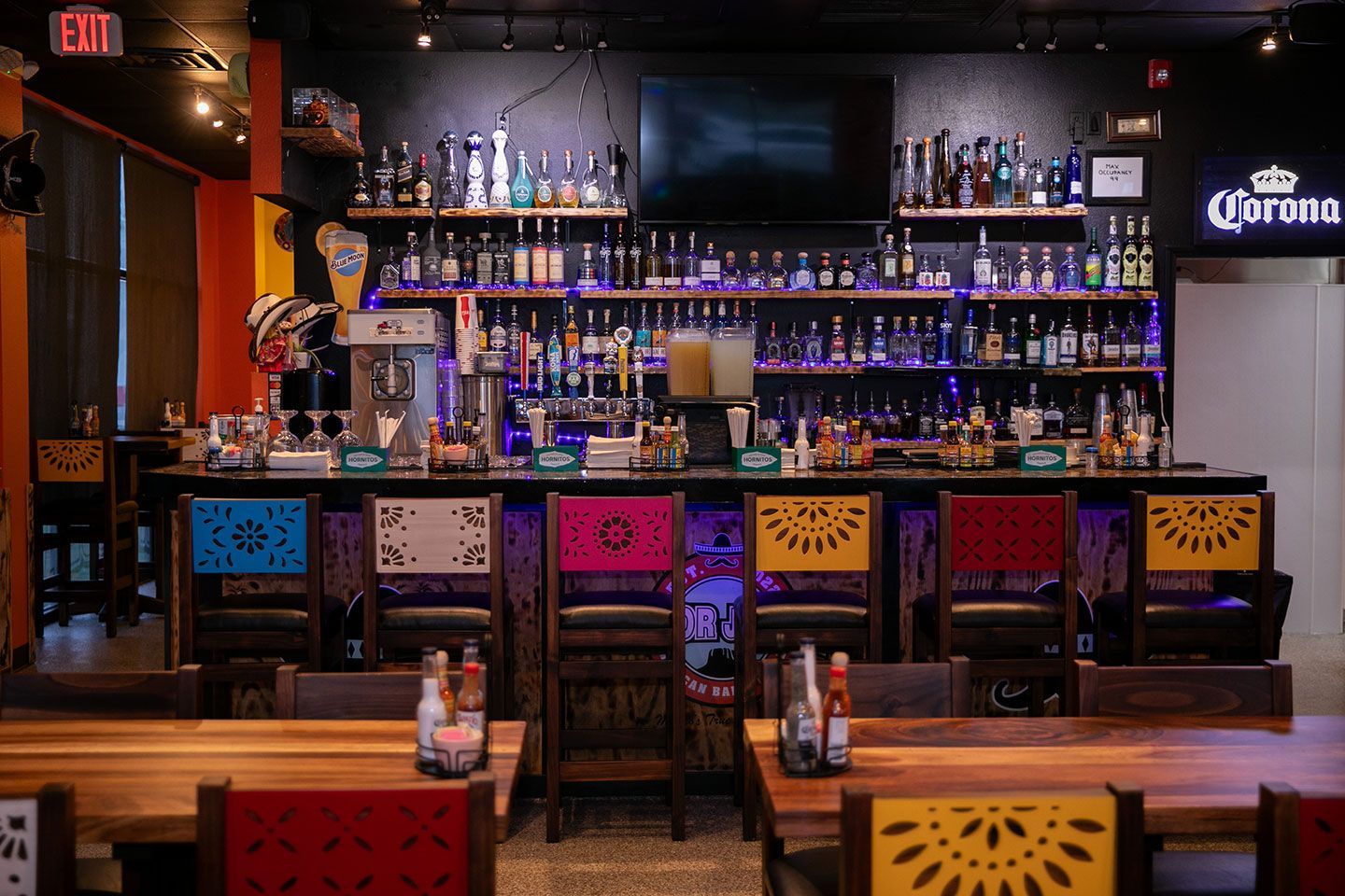 Bar interior with colorful chairs, liquor bottles, and a Corona sign.