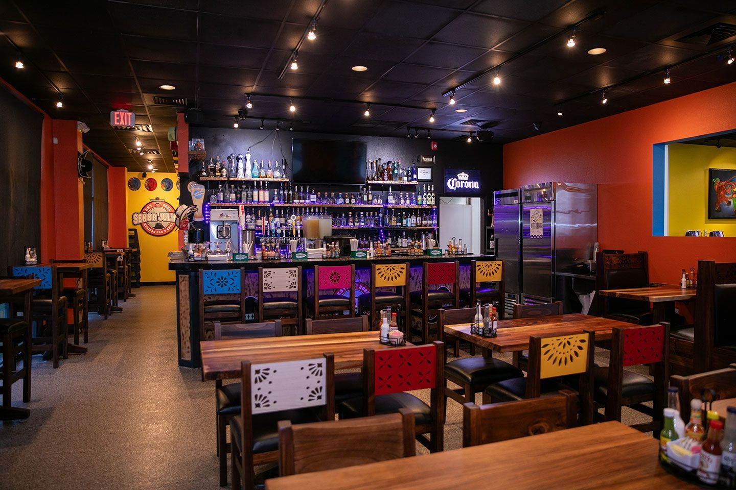 Interior of a Mexican restaurant with a bar, tables, and chairs. Brightly colored walls and decor.