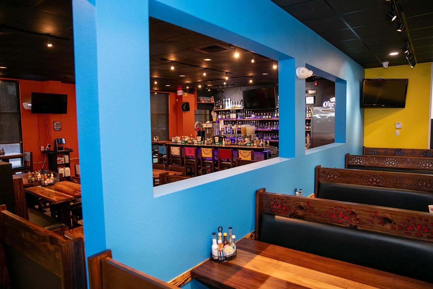 Interior view of a restaurant with booths and a view of a bar, featuring blue, orange, and yellow walls.