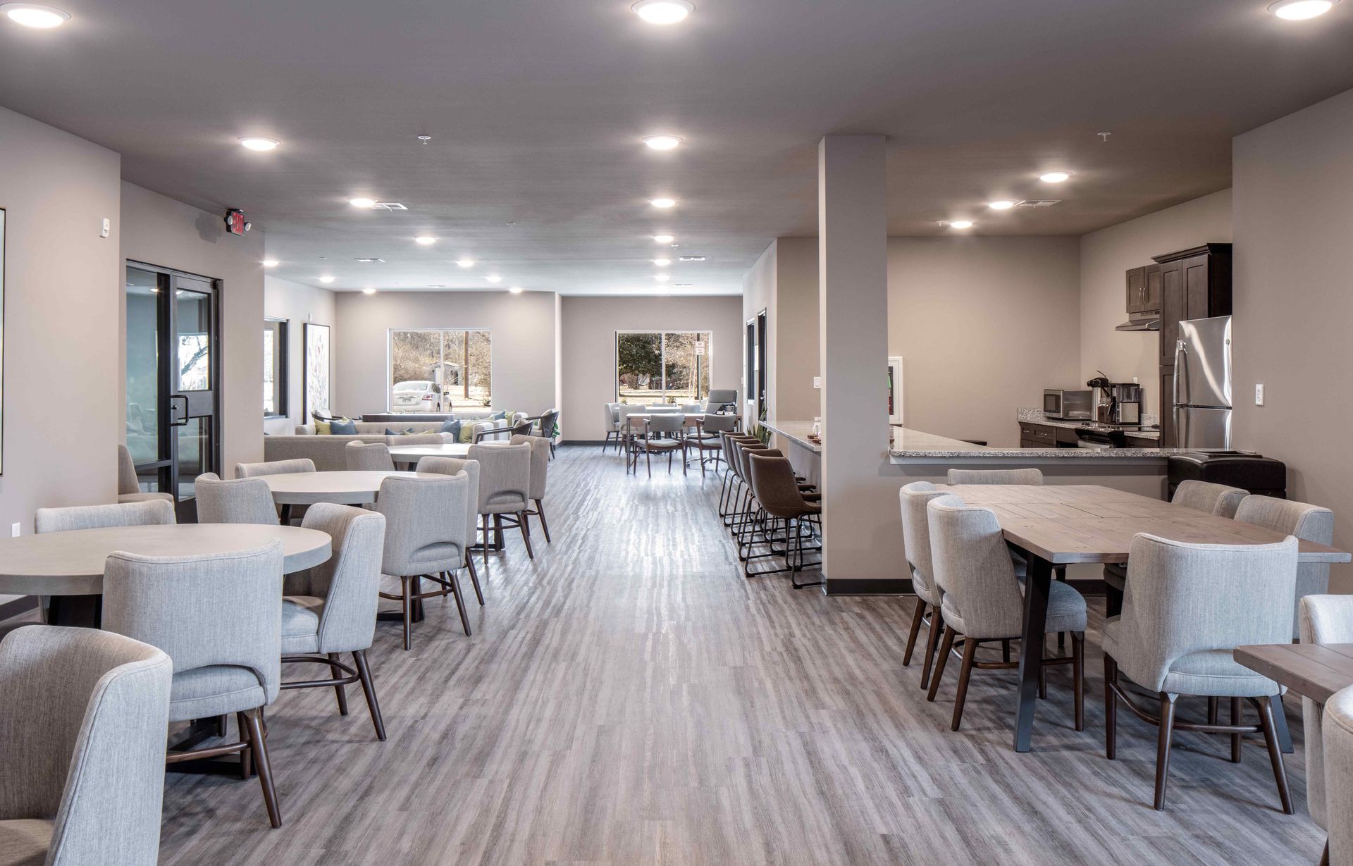 A neutral-toned communal dining area with tables, chairs, and a small kitchen space.