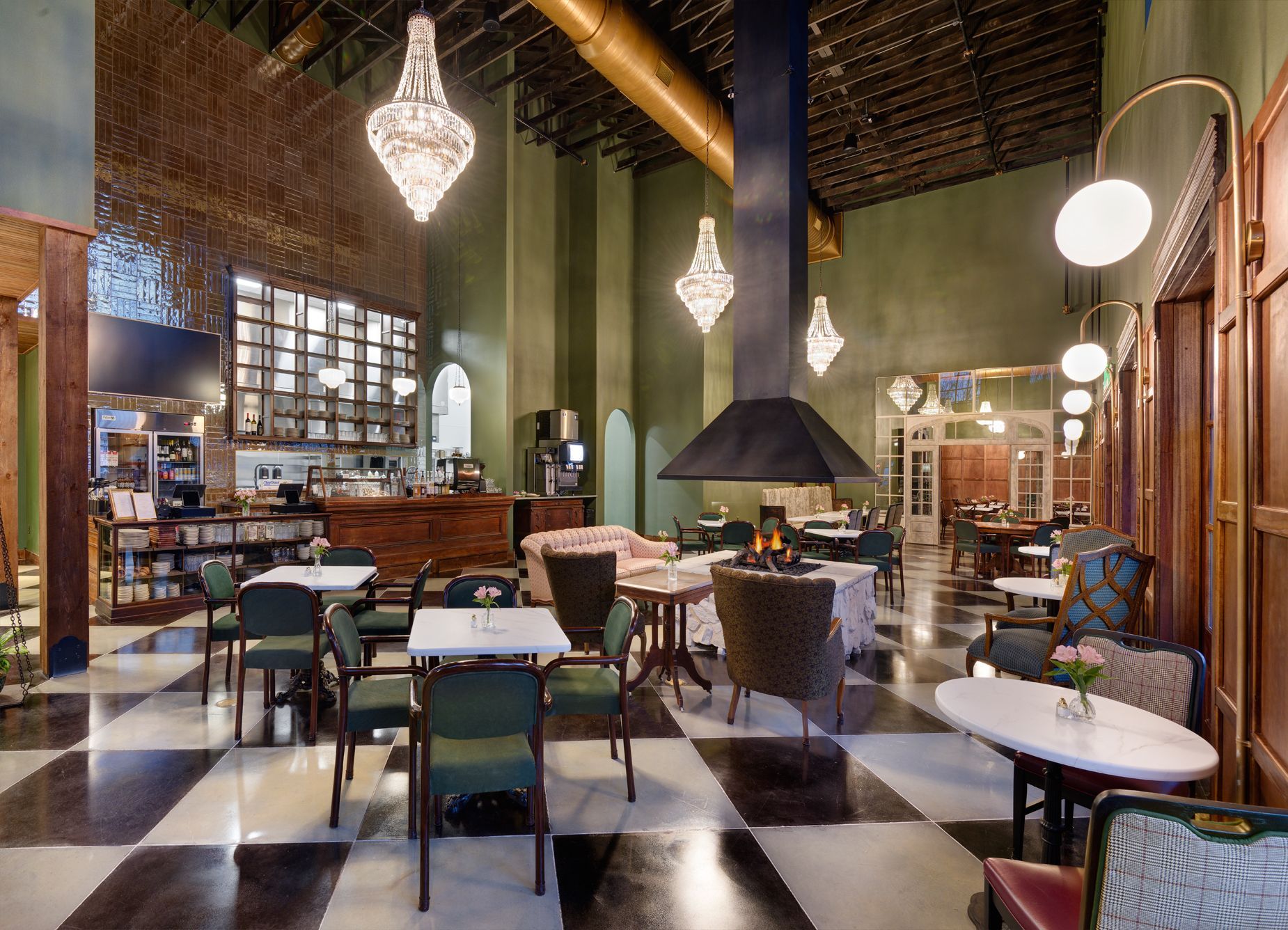 Elegant restaurant interior with a black-and-white checkered floor, green walls, crystal chandeliers, and a fireplace.