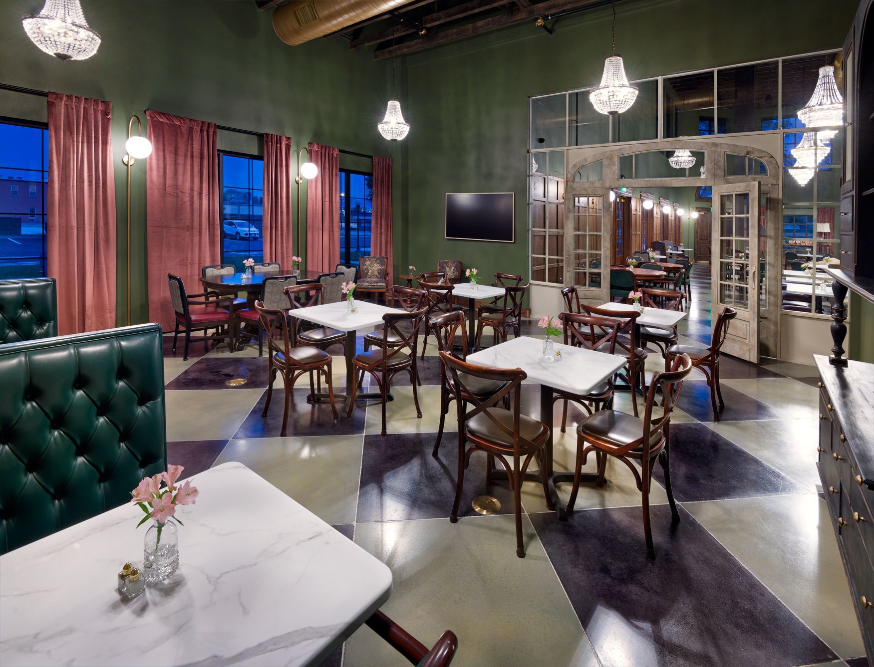 An upscale dining room with marble-topped tables, wooden chairs, green walls, pink curtains, and crystal chandeliers.