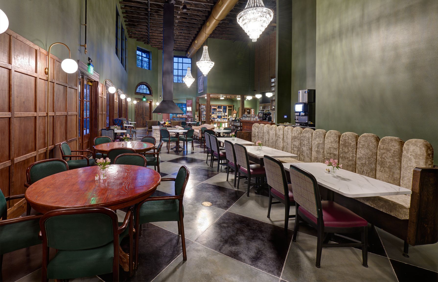 Interior of a restaurant with round wooden tables, a long upholstered booth, and elegant hanging chandeliers.