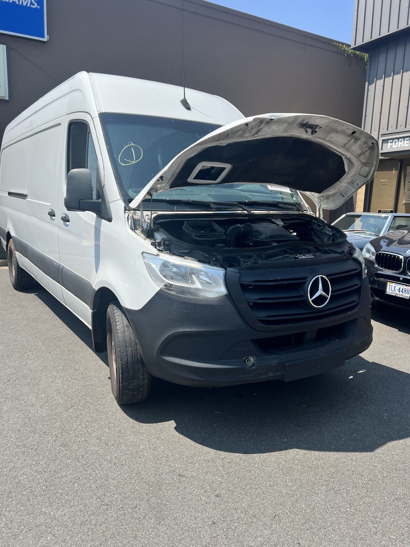 White Mercedes-Benz Sprinter van with its hood open, parked on asphalt.  Daytime outdoor setting.