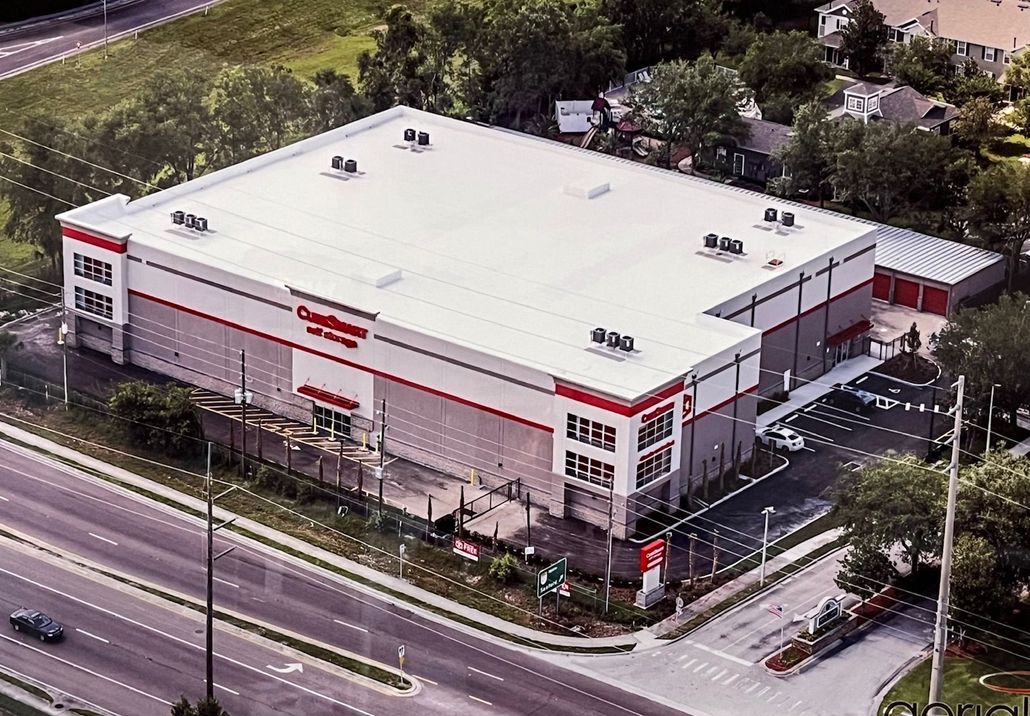 Aerial view of a multi-story CubeSmart self-storage facility with a white roof and gray and red exterior next to a road.