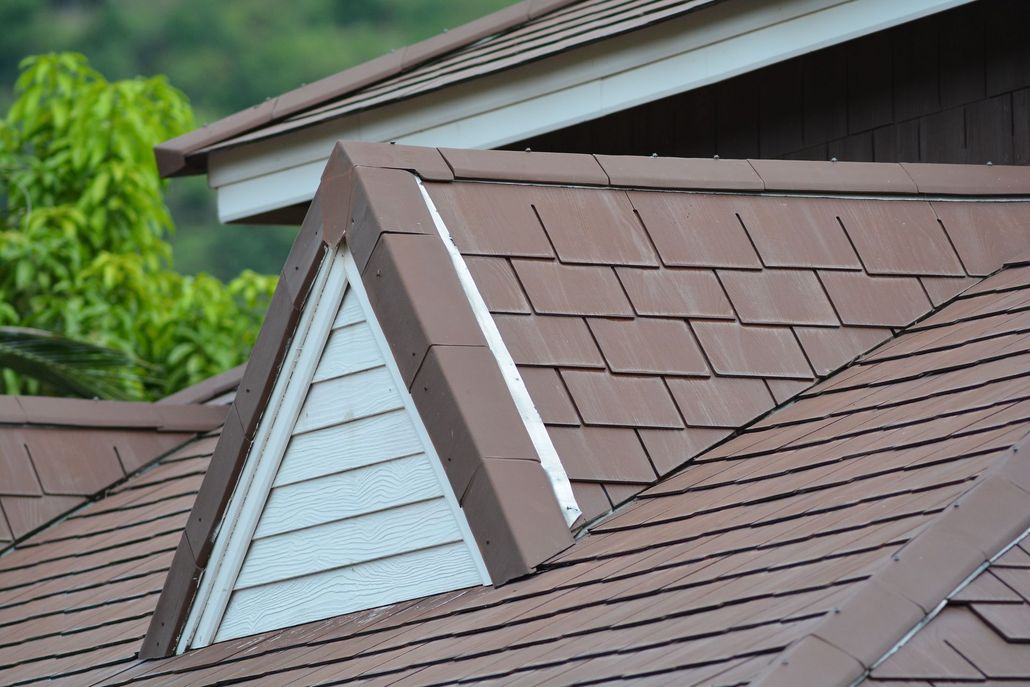 A triangular dormer window set into a brown tiled roof with white siding, under a green-foliaged sky.