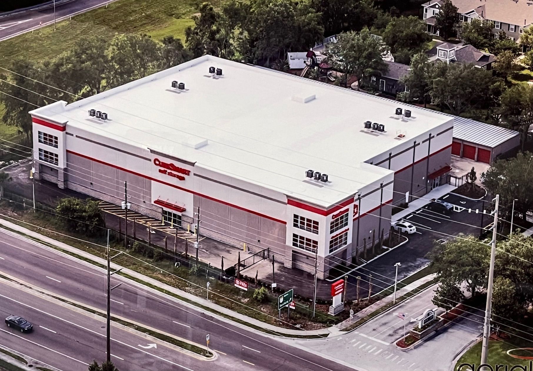 An aerial view of a large, gray and red CubeSmart self-storage building located along a multi-lane road.