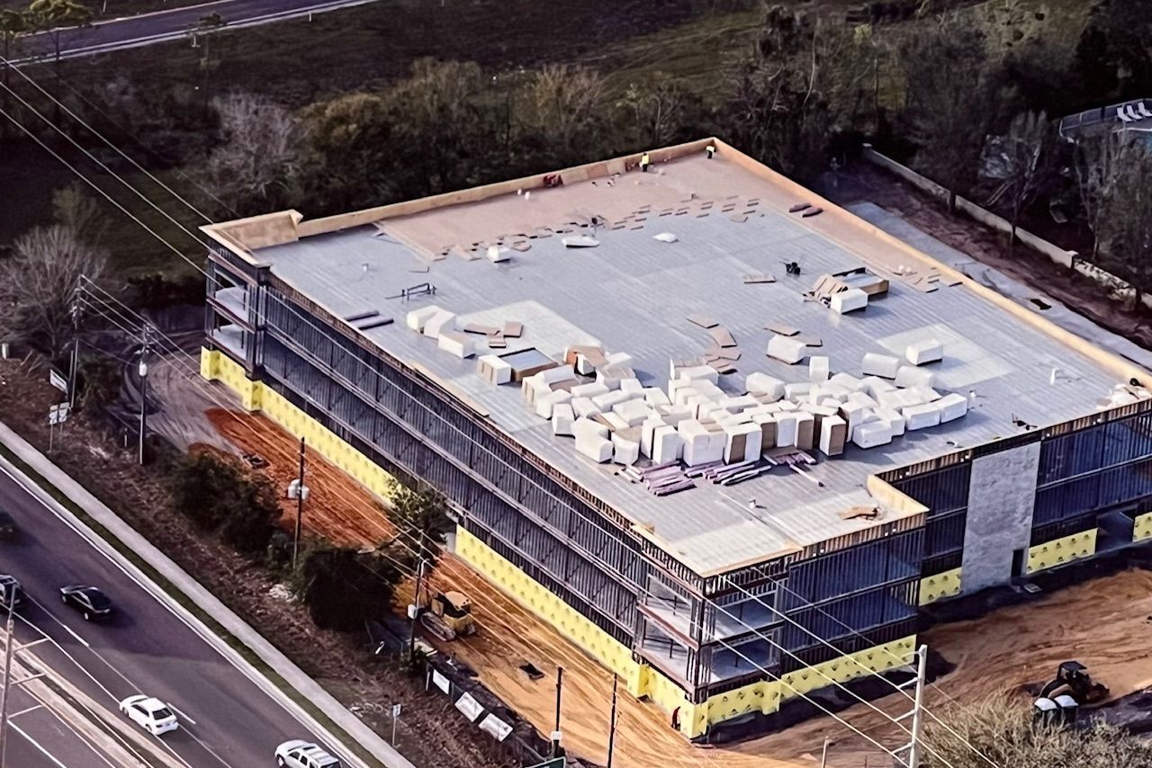 Aerial view of a multistory commercial building under construction with building materials staged on the flat roof.