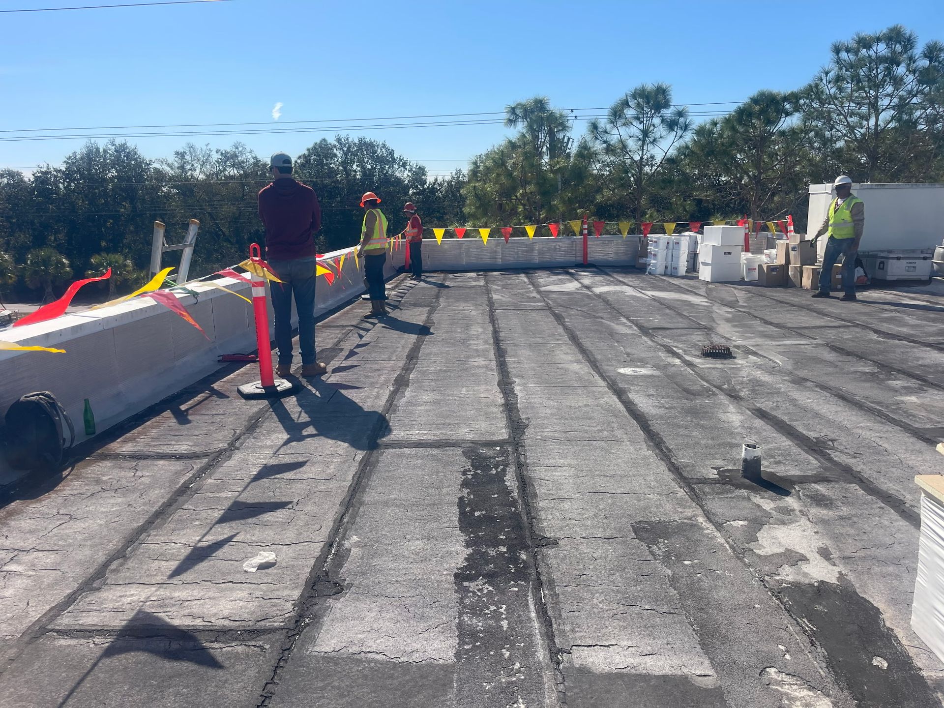 Construction workers on a flat roof marked with flags, under a bright, sunny sky.