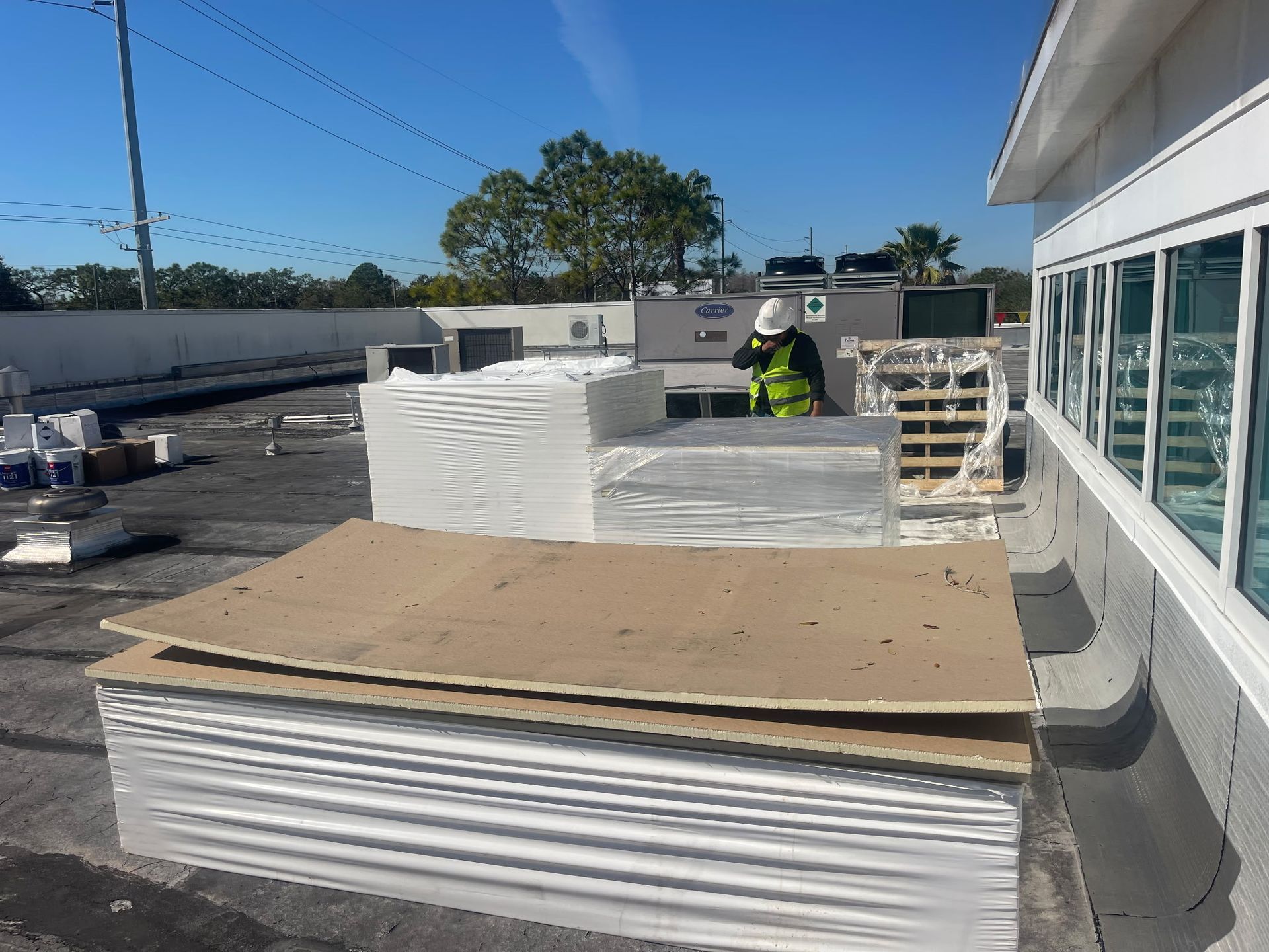 Rooftop scene with worker, construction materials, and commercial building on a sunny day.