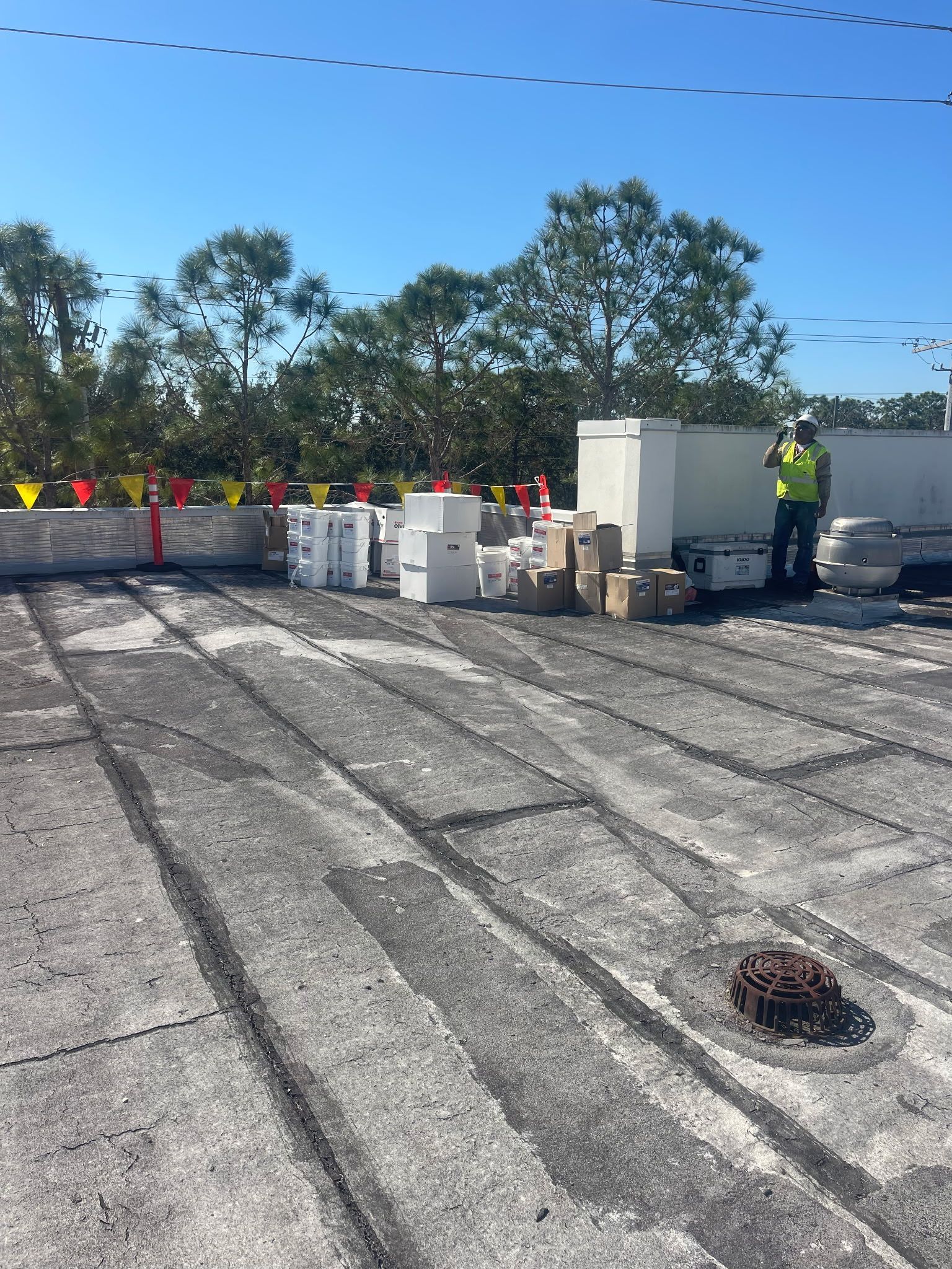 Rooftop with boxes, a worker in a vest, and trees. Sunny day.