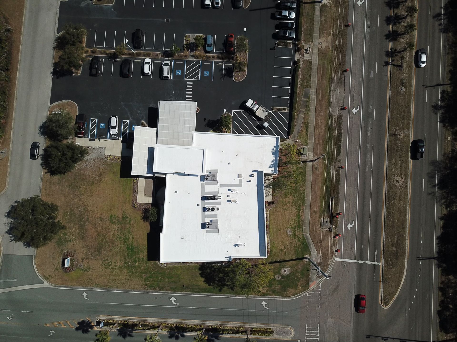 Overhead view of a white-roofed building next to a parking lot and a road with cars.