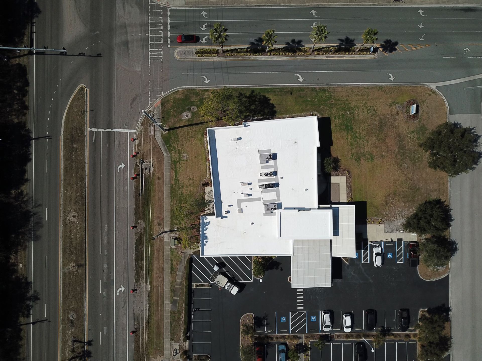 Aerial view of building with white roof, parking lot, and streets.