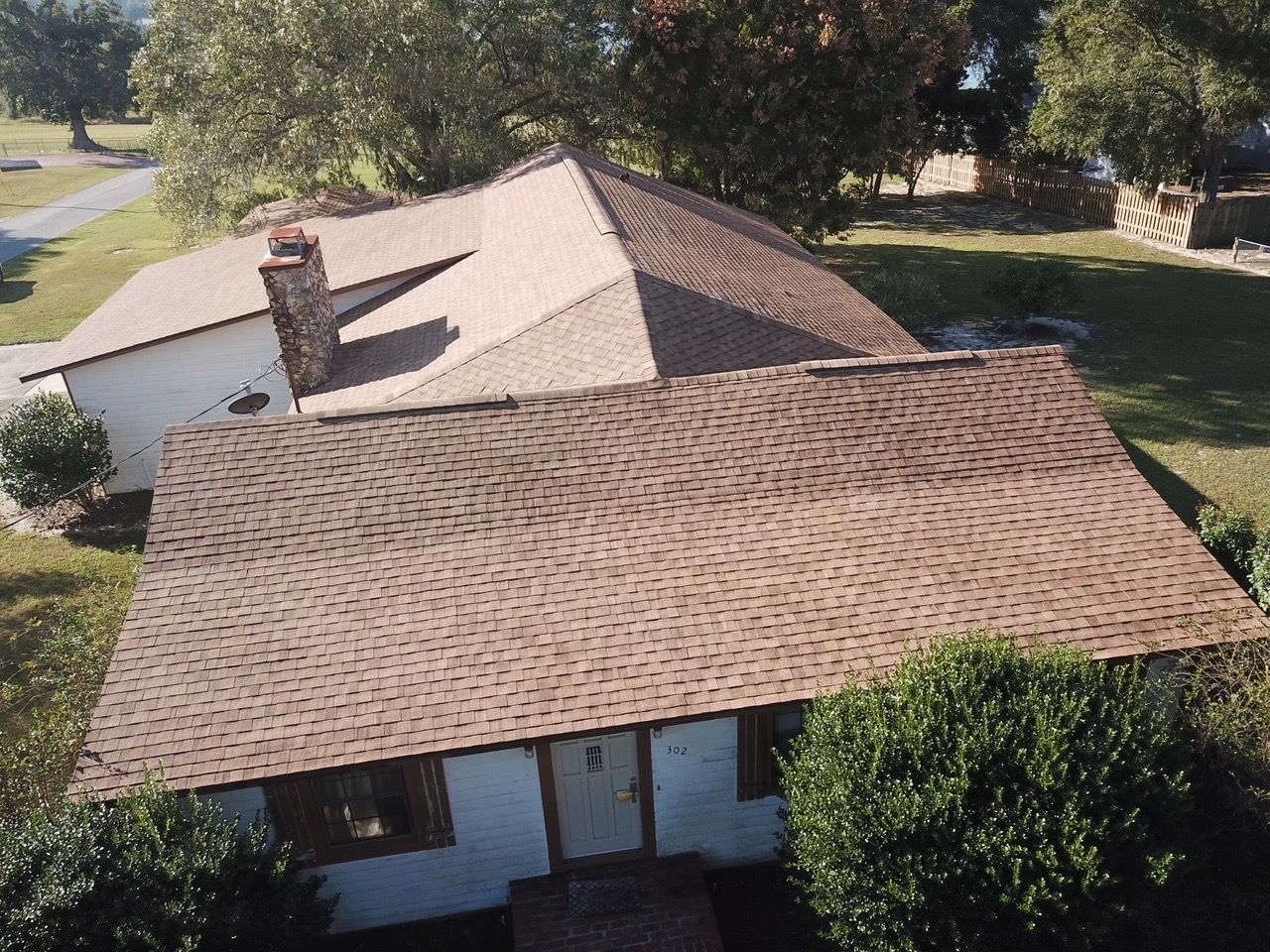 Tan-roofed house with chimney, surrounded by trees and grass, on a sunny day.