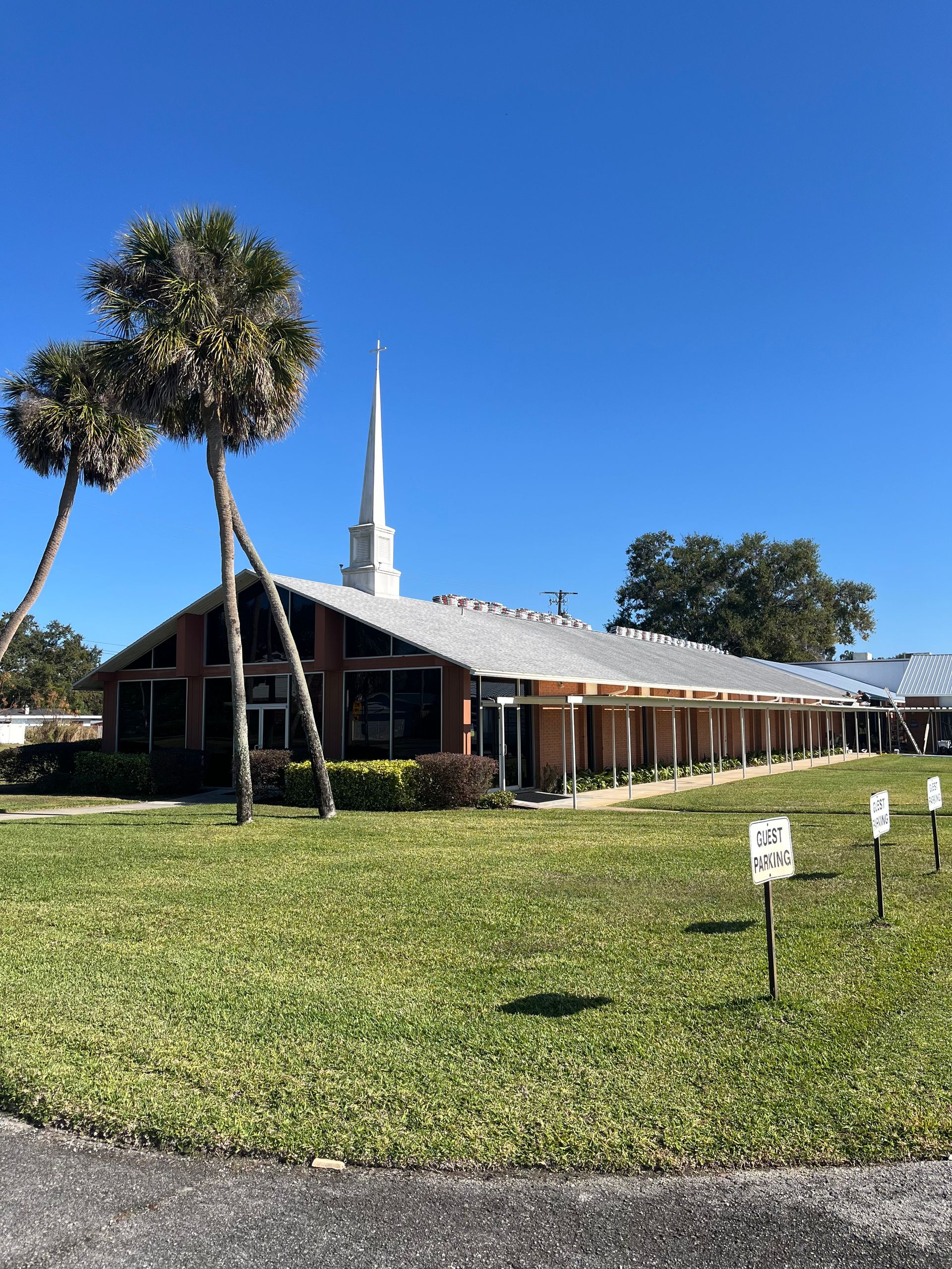 Church building with a white steeple on a sunny day. Palm trees and lawn in front.