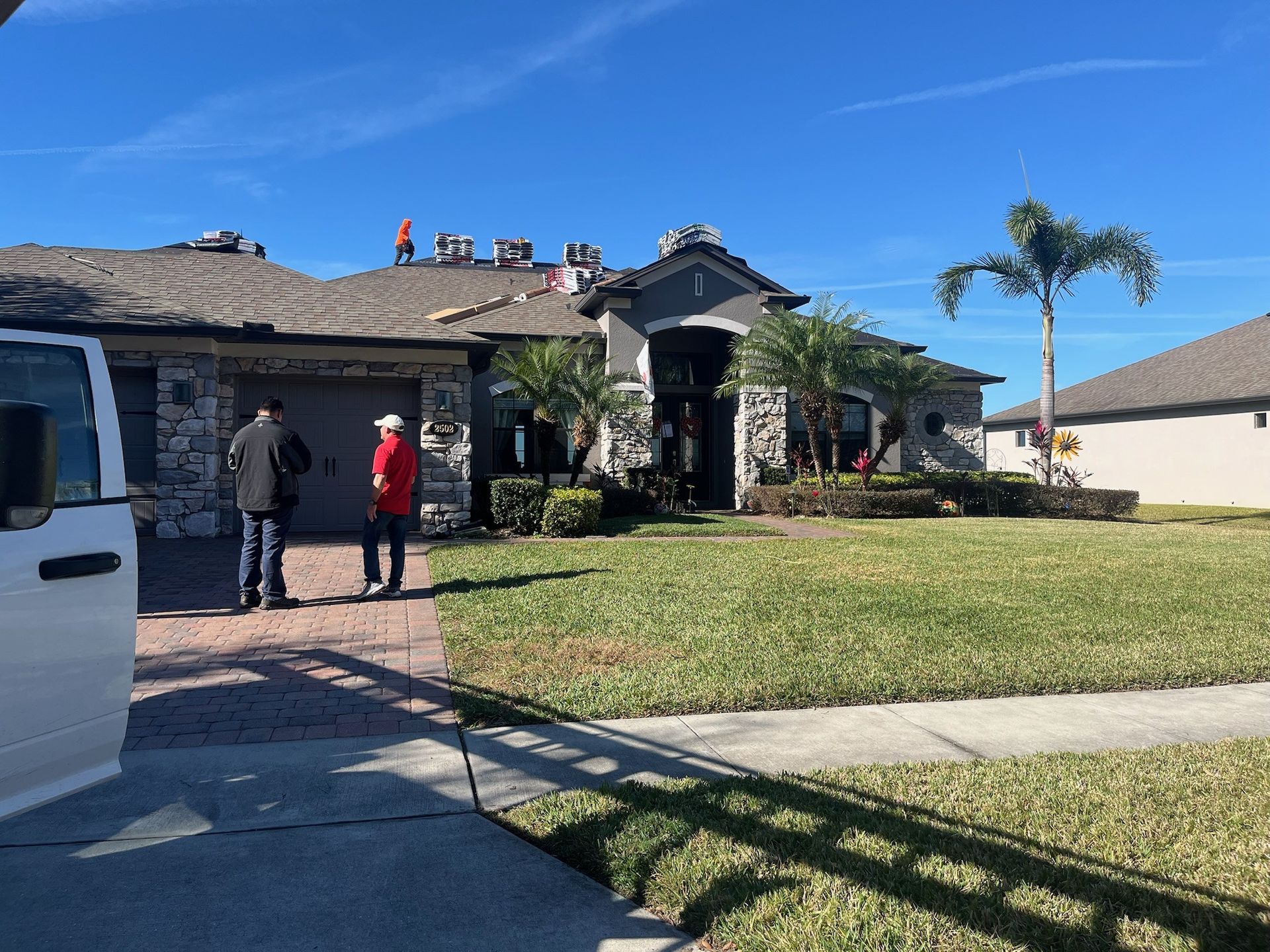 People observing roof work on a house; men in jackets stand on the driveway.