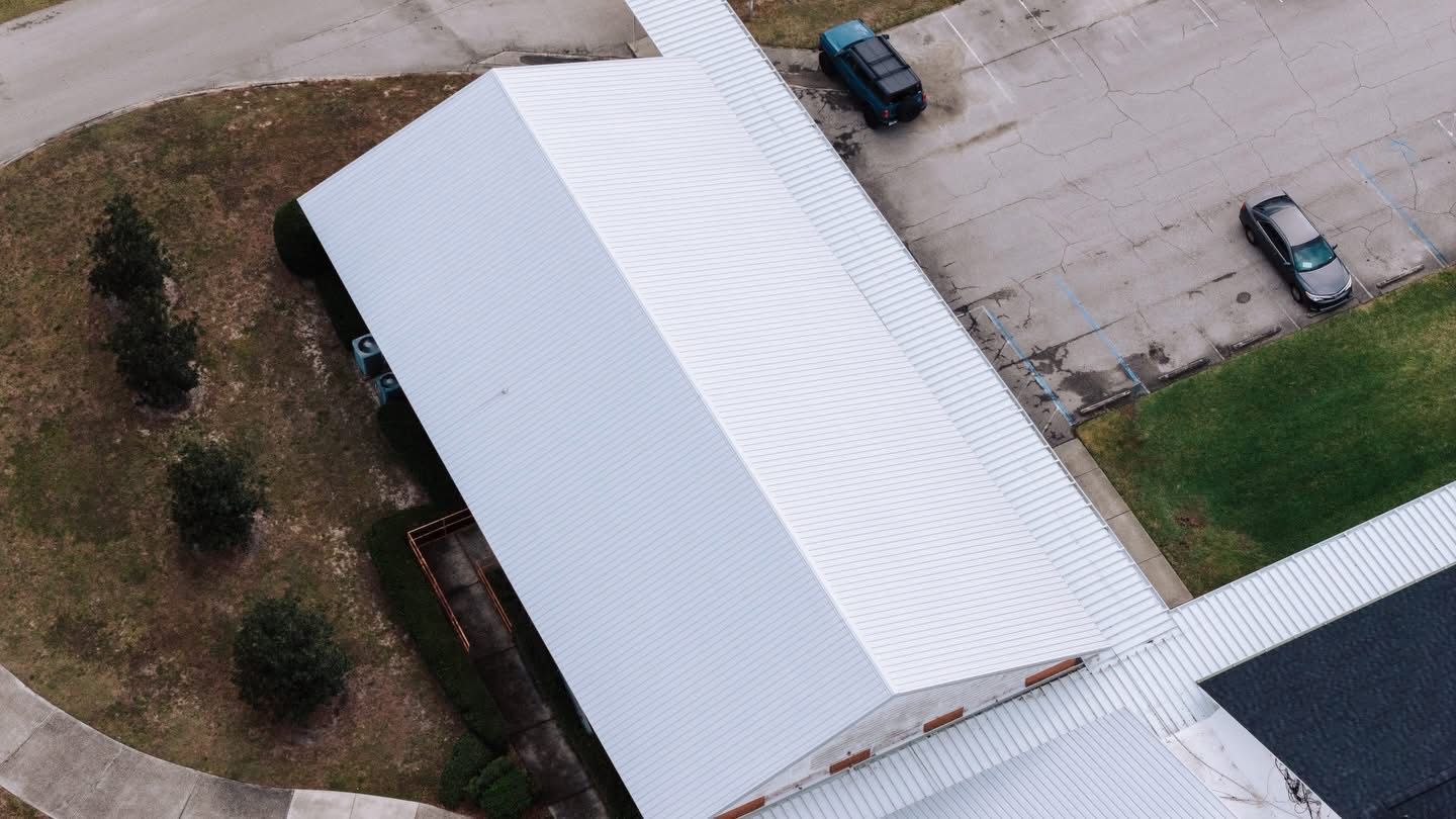 Aerial view of a white metal-roofed building with several parked vehicles.
