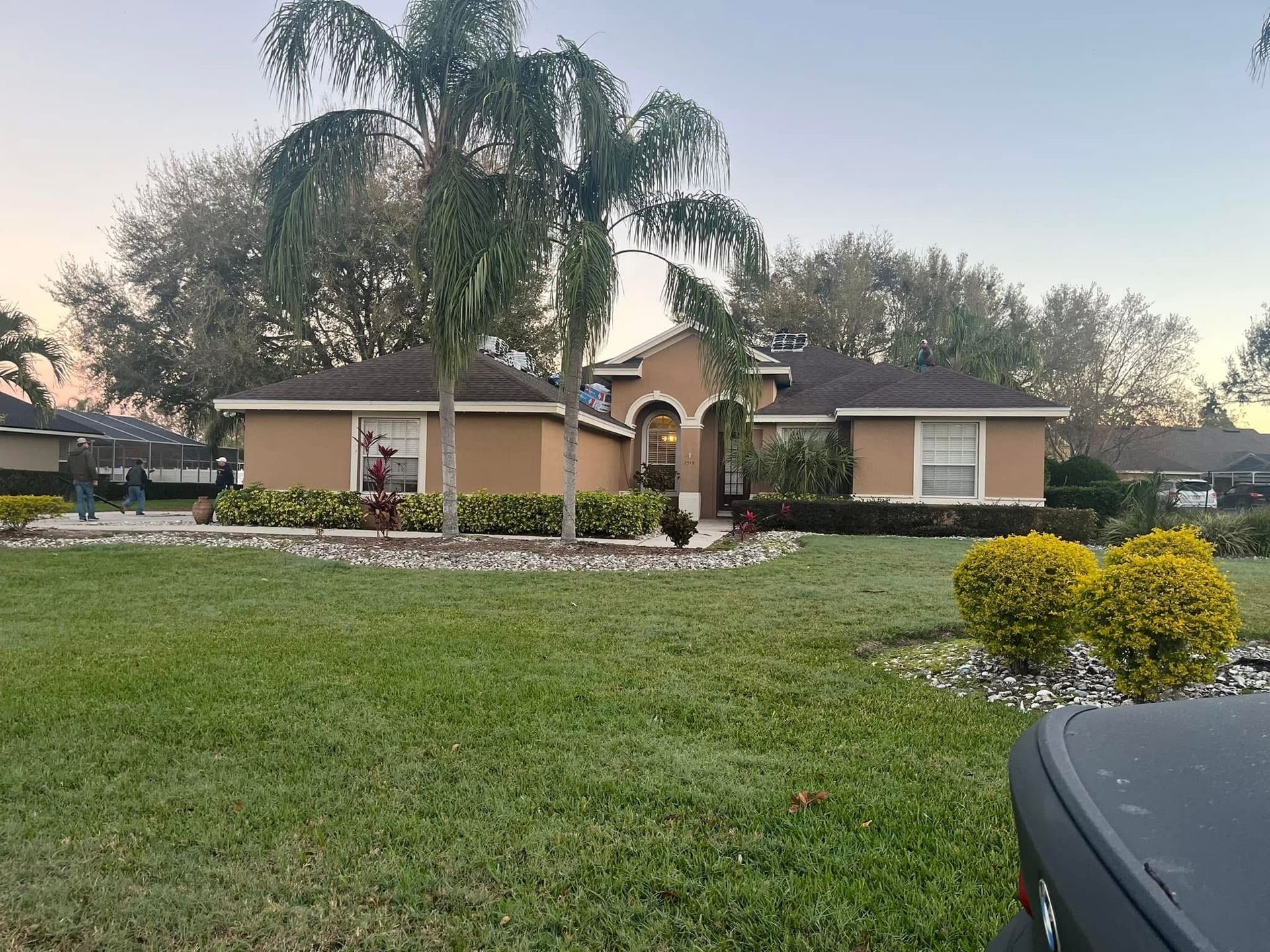Tan house with palm tree and bushes in front lawn.