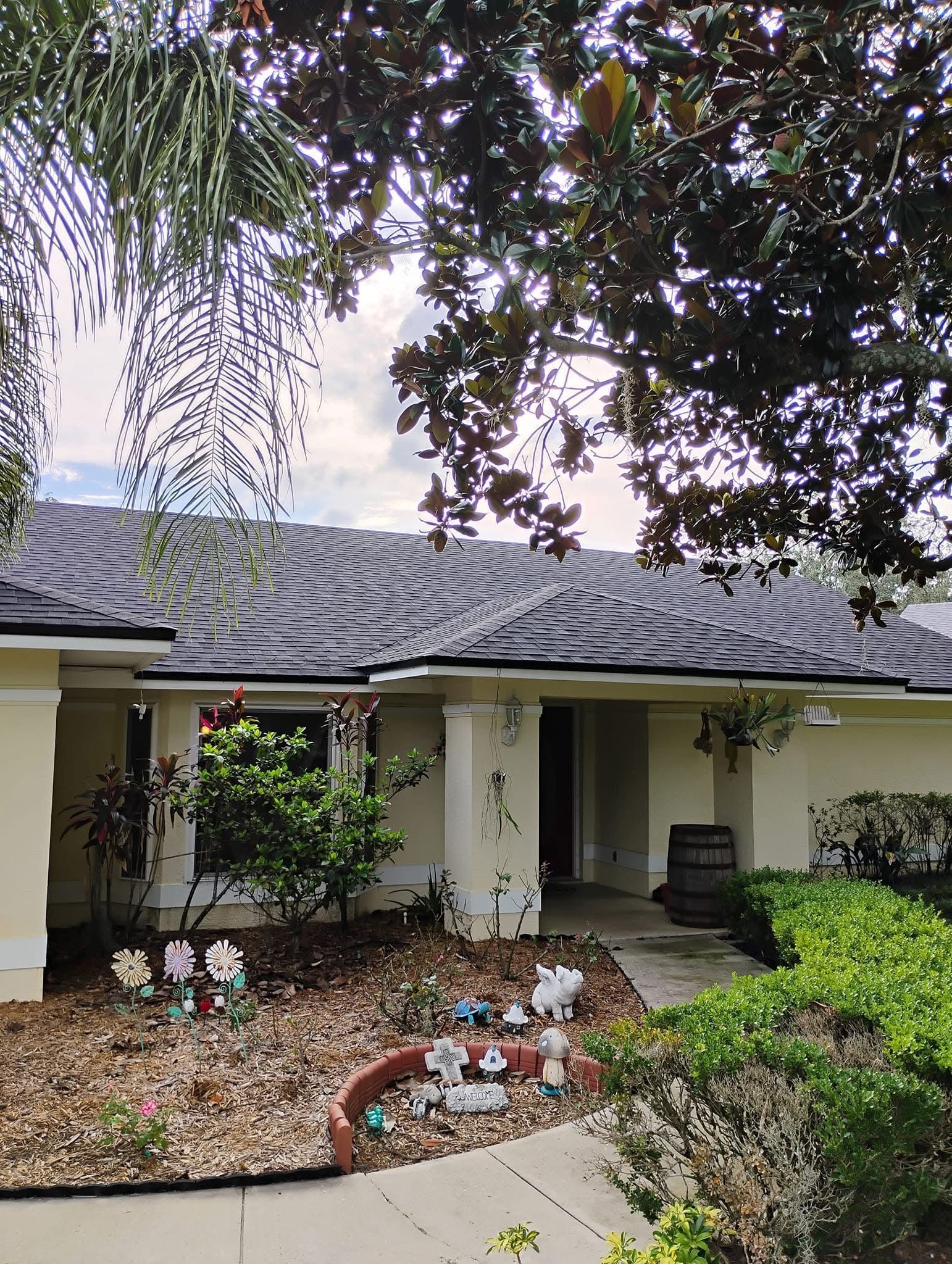 Front of a light-colored house with dark roof and landscaping, sunny day.